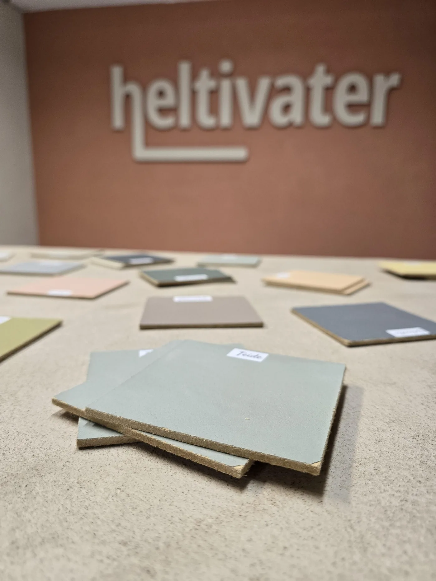 Fargeprøver i mikrosement på bordet i showroomet til Heltivater, med logoen på veggen bak